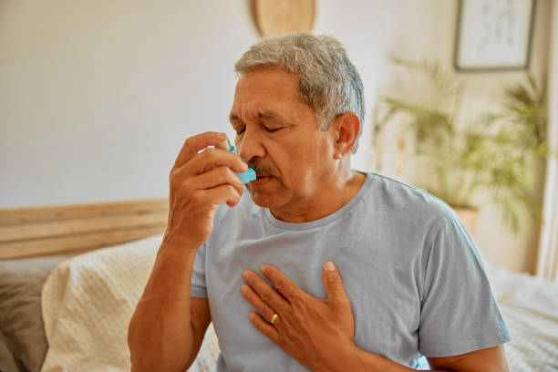 Asthma, breathing and medicine with old man in bedroom for stress, chest pain and emergency. Asma, allergy and lungs medication with senior male and spray at home for healthcare, disease and oxygen asma, respiración y medicamentos con el anciano en el dormitorio de la casa para el estrés, el dolor en el pecho y la emergencia. medicamentos para ataques, alergias y pulmones con hombres mayores y aerosoles para atención médica, enfermedades y oxíge