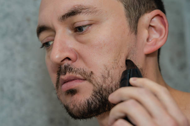 istock Handsome man shaving his beard by electric razor 1488642832