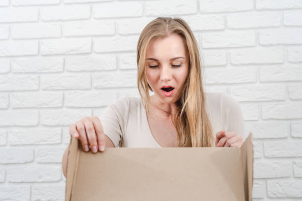 istock Young blonde woman looking in a box with white brick background 1488642838