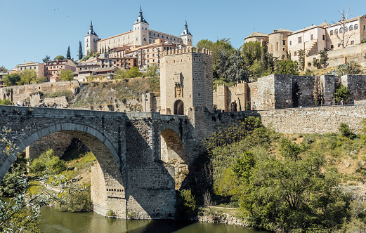 Panoramic cityscape of Toledo with Alcantara bridge over Tagus river, the city wall and the Alcazar. Castilla La Mancha, Spain