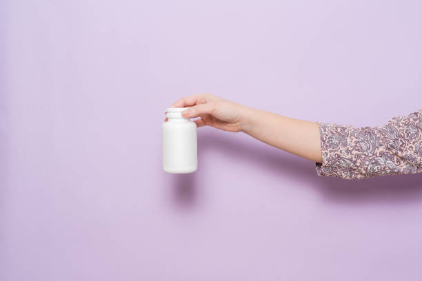 istock White plastic bottle in female hand in lilac background. Packaging for pills, capsules or supplements. 1488643041