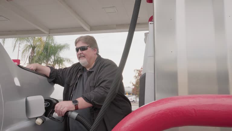 One Mature Caucasian Man Using a Gas Pump to Fuel a Silver Pickup Truck on an Overcast Day in California, USA