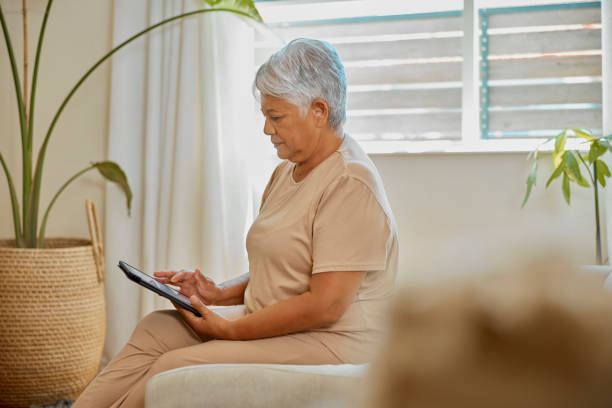 senior woman, relax and tablet on sofa for reading, typing or social media app in home living room. elderly lady, mobile touchscreen and chat on internet, blog or web for news, article or information - newspaper the media digital tablet digitally generated image imagens e fotografias de stock