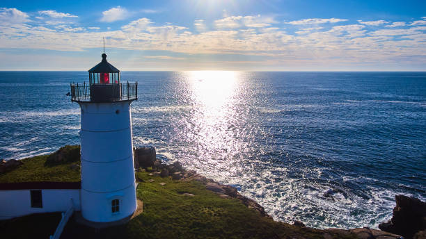 antenne hinter dem leuchtturm auf einer insel in maine mit sonnenlicht, das den ozean bedeckt.jpg - maine lighthouse york maine new england stock-fotos und bilder