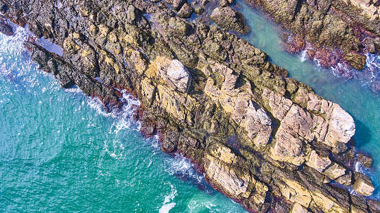 Image of Aerial down of rocky coast section with crashing waves