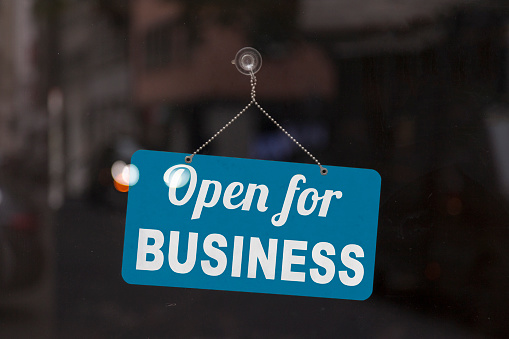 Close-up on a blue open sign in the window of a shop displaying the message: Open for business.