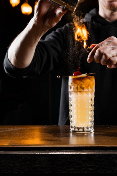 istock Burning cinnamon in cocktail. Bartender pours and fire burns cinnamon in alcoholic cocktail at a bar. Bartender is preparing alcoholic cocktail with whiskey, fresh lemon, sugar syrup and egg white. 1488645415