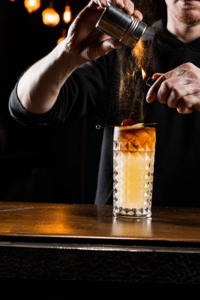 istock Burning cinnamon in cocktail. Bartender pours and fire burns cinnamon in alcoholic cocktail at a bar. Bartender is preparing alcoholic cocktail with whiskey, fresh lemon, sugar syrup and egg white. 1488645417