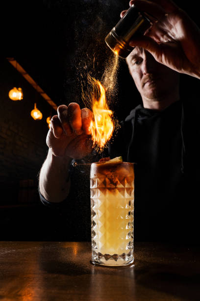 istock Burning cinnamon in cocktail. Bartender pours and fire burns cinnamon in alcoholic cocktail at a bar. Bartender is preparing alcoholic cocktail with whiskey, fresh lemon, sugar syrup and egg white. 1488645419