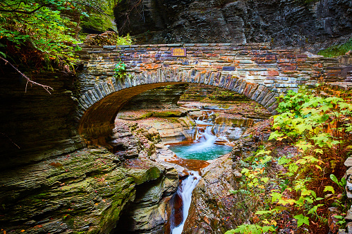 Image of Beautiful stone arch walking bridge over gorge and river with blue waters and waterfalls during fall