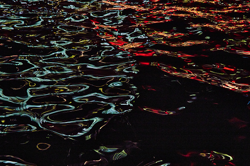 Image of Blue and red lights reflecting off waves of water in river