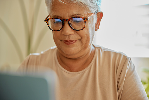 Online, reading and senior woman in living room with glasses, content and browsing the internet. Ebook, website and elderly female relax with social media, news or entertainment app and subscription