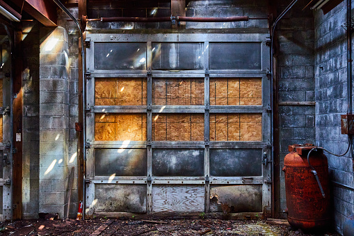 Image of Detail of abandoned interior mechanic shop with gray garage door and red canisters