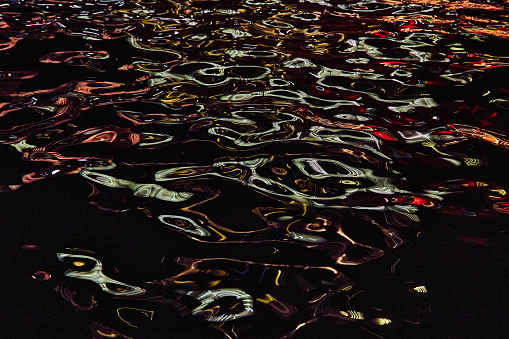 Image of Detail of river at night with blue and red lights reflecting on highlights