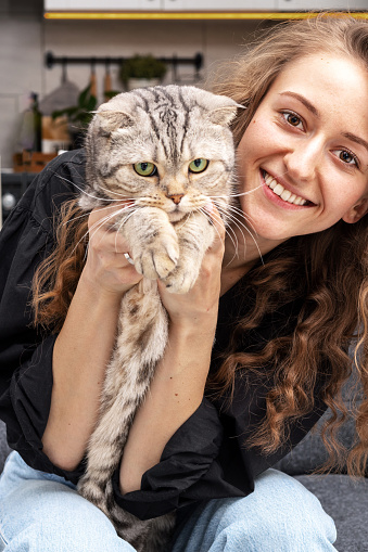 Young smiling woman with holding her Scottish breed cat in her hands.