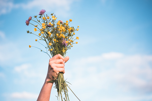 A hand holds a bouquet of flowers in the air against a blue sky.