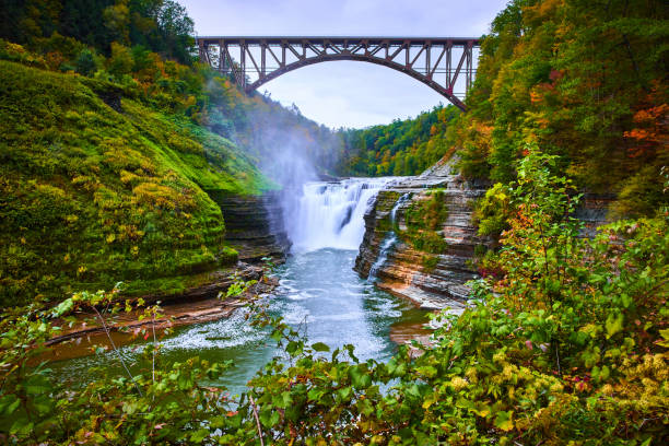 istock Huge waterfall in New York carves through rocky mossy cliffs with greenery in early fall and large arched steel train track bridge above.jpg 1488664411