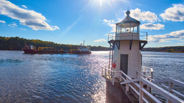 Large commercial ship on Maine river sails past small lighthouse with blue skies.jpg Image of Large commercial ship on Maine river sails past small lighthouse with blue skies bilge of ship stock pictures, royalty-free photos & images