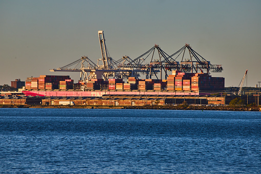 Image of Large ship full of shipping containers loading on coast of New York City in golden hour light