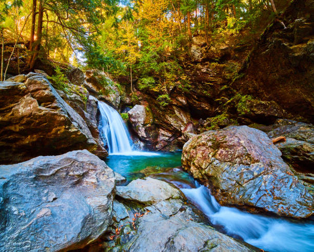 Image of Magical blue waterfall pouring into pool of water surrounded by vibrant fall forests and gorge cliffs