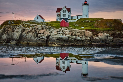 Image of Maine lighthouse reflects off of puddle with morning light