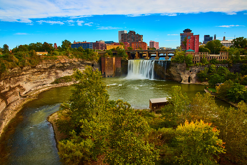 Image of Rochester skyline along river and cliffs with waterfall pouring past bridge