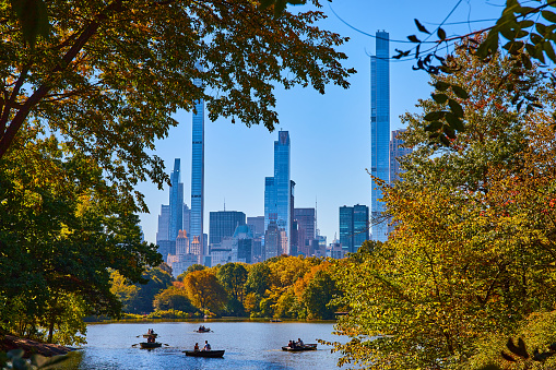 Image of Skyscrapers surround Central Park New York City looking through trees at pond with boat