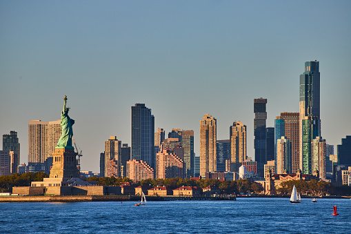 Image of Statue of Liberty with skyscrapers surrounding from waters in golden light