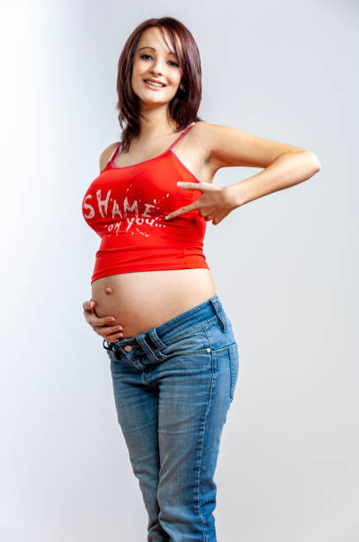 pregnant young woman with brown hair in jeans and sleeveless top showing her big belly.