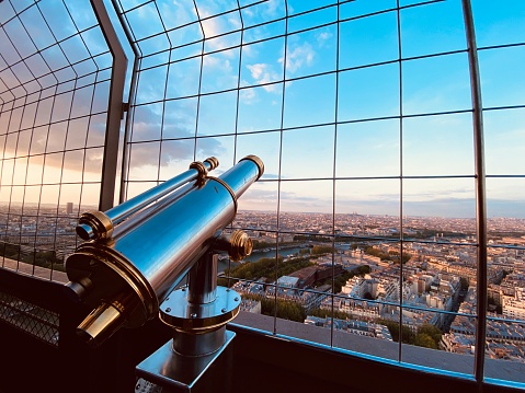 The telescope stands on the bank of River. The pipe is in focus, and the shore opposite is out of focus. Blue sky, clouds, spyglass in blurred focus, other shore in focus. Viewing through the tube for the entertainment of citizens walking along the embankment