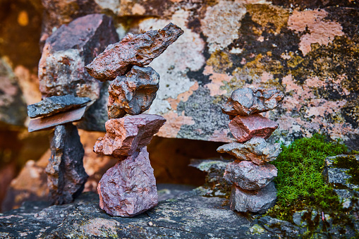 Image of Trio of small cairn stone stacks resting on lichen-covered rocks by wall