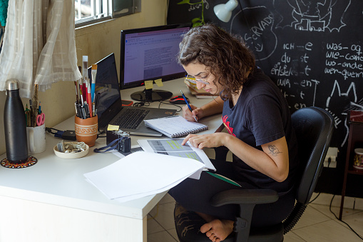 young girl looks at her notes amid the study bench full of papers