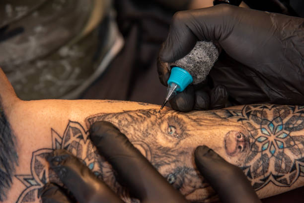 Professional tattooer doing tattoo on hand using tattoo machine in studio