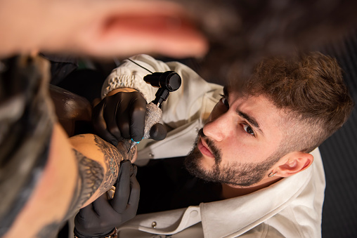 Professional tattoo artist makes a tattoo on the client's hand close-up. Hands in white gloves written out the body of a girl art print