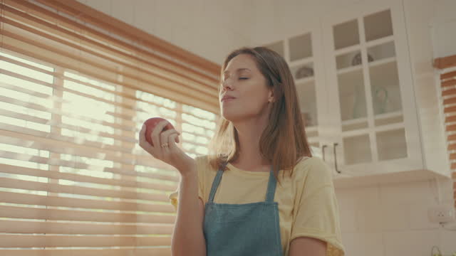 Scene of Caucasian young adult woman eating apple at home