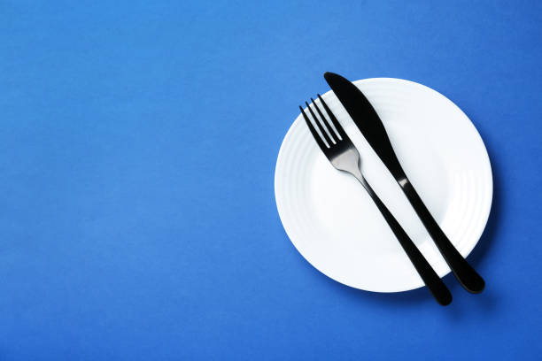 istock Clean white plate with cutlery on blue background, top view. Space for text 1488704628