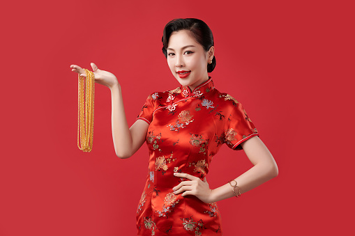 Chinese new year festival, Beautiful Young asian woman wearing traditional cheongsam qipao dress with gold necklaces on red background,