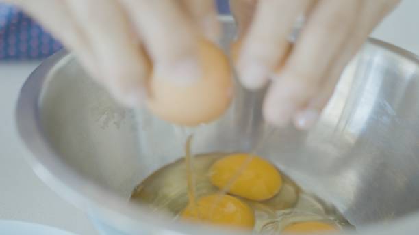 gros plan d’œufs fêlés dans un bol, femme âgée cuisinant à la maison, vie active de retraite âgée - break eggs domestic kitchen breaking photos et images de collection