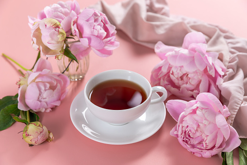 Feminine floral composition. Cup of tea and pink peonies flowers on pink background.