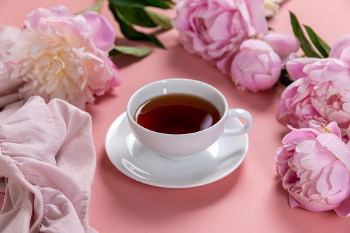 Feminine floral composition. Cup of tea and pink peonies flowers on pink background.