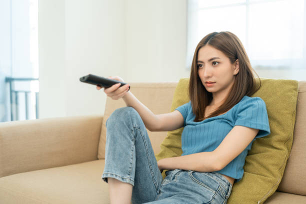 istock Happy Young asian woman watching television using remote to change the program menu. Very enjoy and excited TV menu. Sitting in living room relaxing on the couch. 1488733217