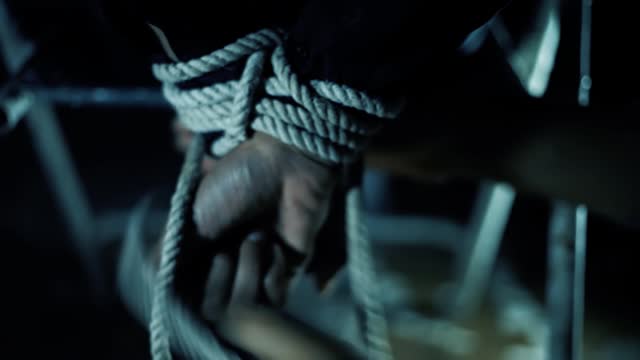 Close-up shot of a man untieing a hostage, dark light. HD footage.