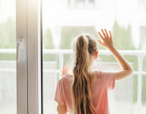 istock Sad little girl looking through  window at home. 1488739917