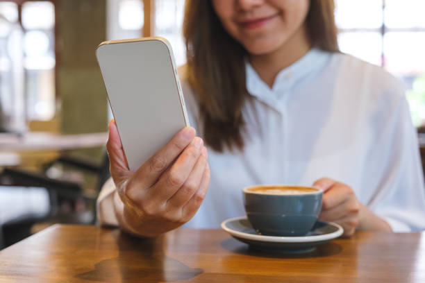 istock Closeup image of a young woman holding and using mobile phone while drinking coffee in cafe 1488743526