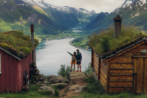 Happy female and male hiking  in the mountains to a view of authentic viking town and the fjord from above in Rakssetra, Stryn, Western Norway