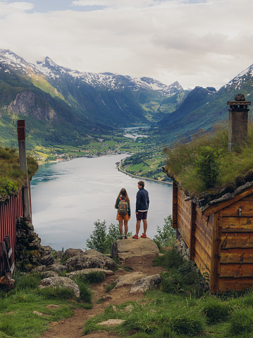 Happy female and male hiking  in the mountains to a view of authentic viking town and the fjord from above in Rakssetra, Stryn, Western Norway