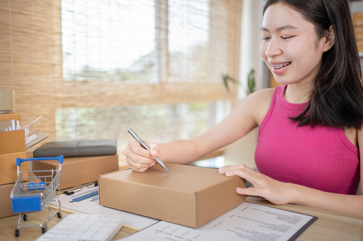 Woman is writing down the customer's details and addresses on the notebook or post box in order to prepare for shipping according to the information, Packing box, Sell online, Freelance working.