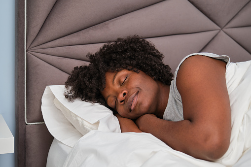 Happy african young woman sleeping on white sheets in bed. Resting asleep.