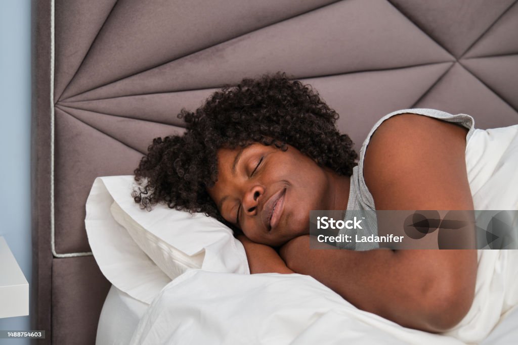 Happy african young woman sleeping on white sheets in bed. Happy african young woman sleeping on white sheets in bed. Resting asleep. Sleeping Stock Photo