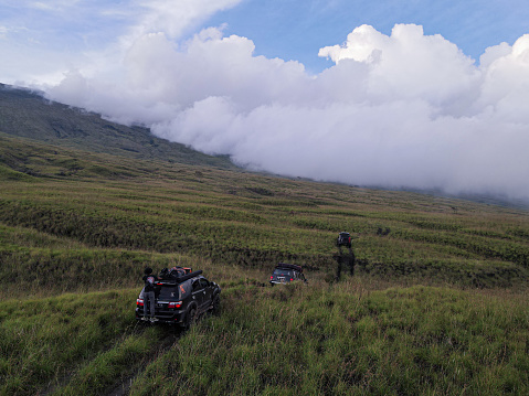 Drone view 4 offroad cars passing through the vast Tambora savanna in the late afternoon before sunset on an overland trip